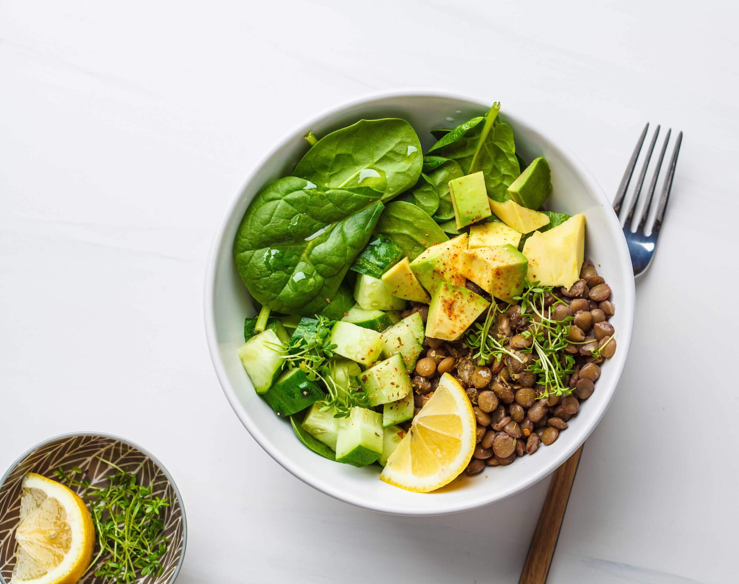 Bowl mit braunen Linsen, Blattspinat, Avocado und einer Scheibe Zitrone.